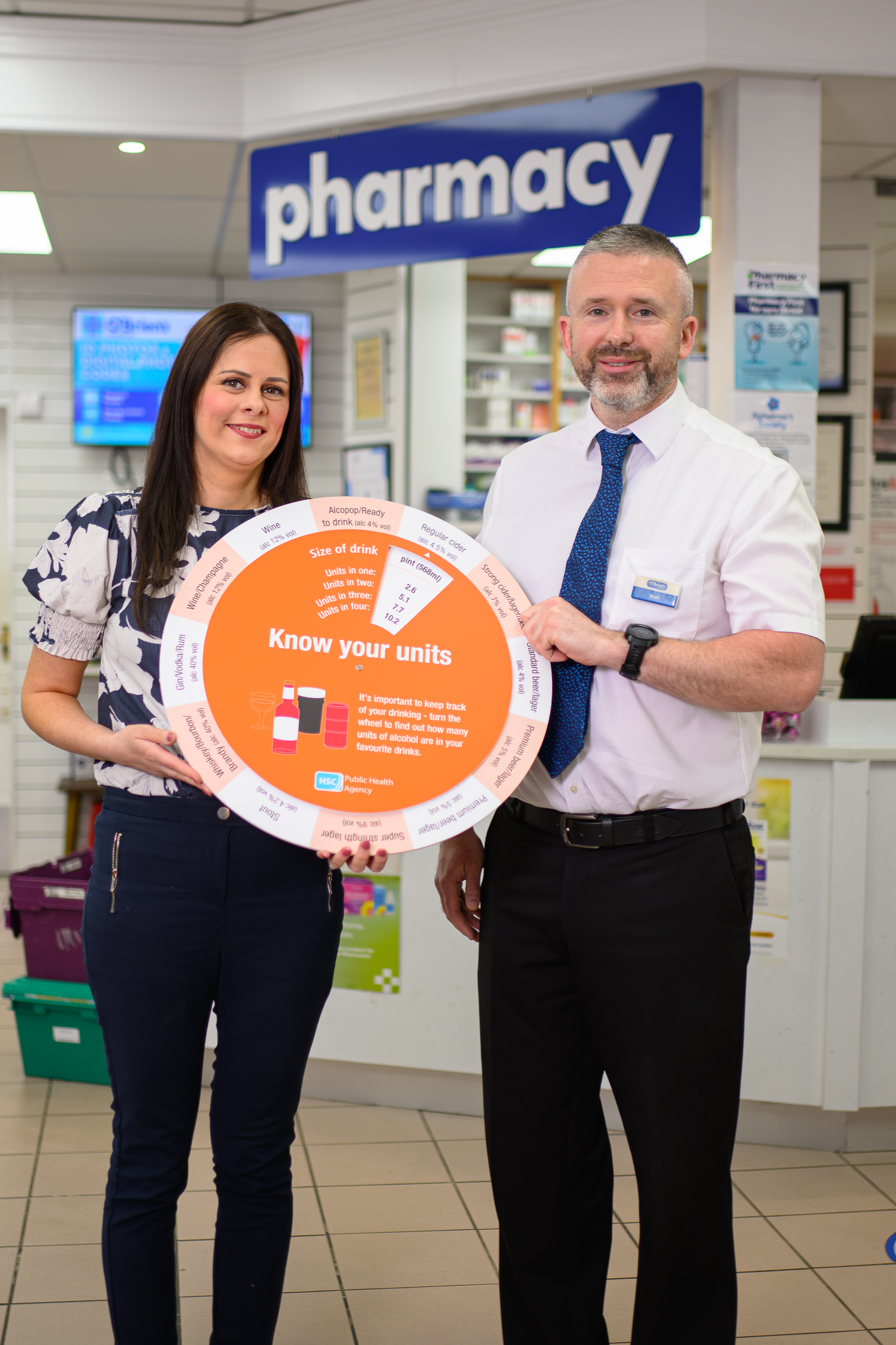 Photograph of PHA rep and pharmacist holding the 'know your units' alcohol wheel in pharmacy. 