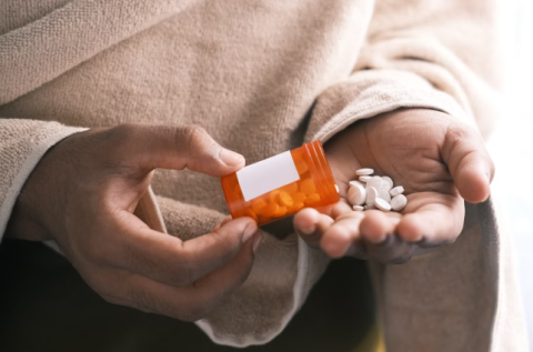 hand holding a bottle of pills spilled over to another hand