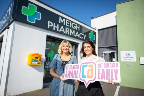 Photograph of Dr Anna Cullen and Clare Conroy (pharmacist) standing outside Meigh pharmacy, holding a 'Be Cancer Aware' sign