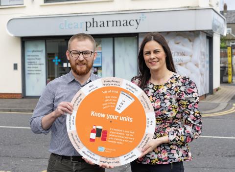 Photograph of PHA rep and pharmacist, holding the 'know your units' campaign unit calculator wheel, outside Clear Pharmacy in Bangor.