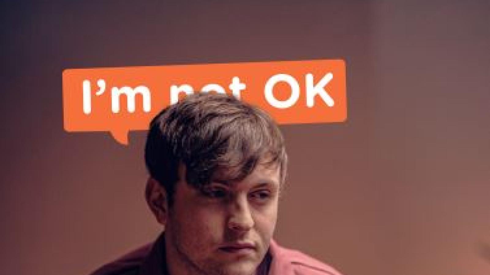 Campaign poster showing a man in his 20s with word behind him "I'm not ok" with the word "not" slightly hidden.