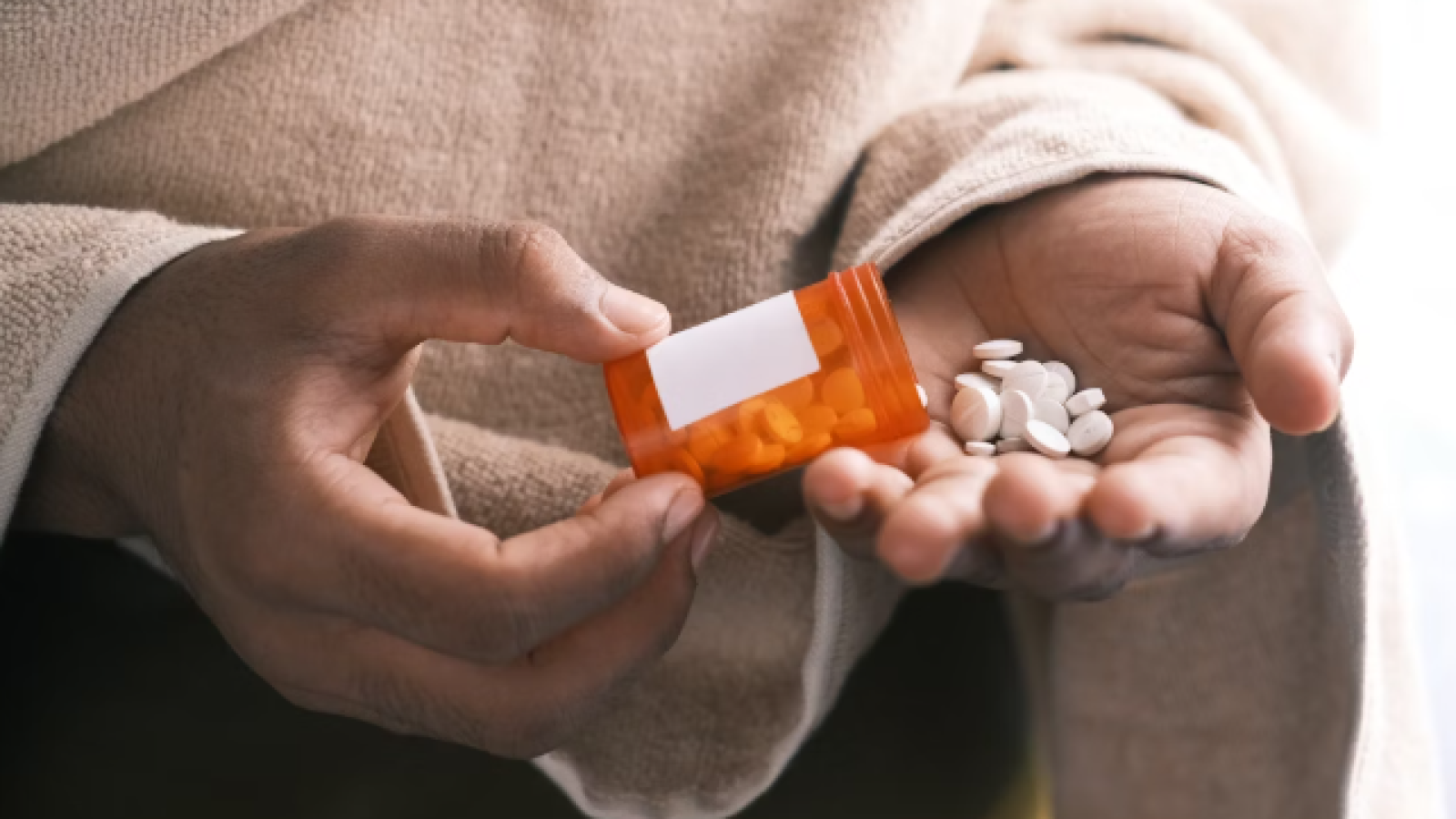 hand holding a bottle of pills spilled over to another hand