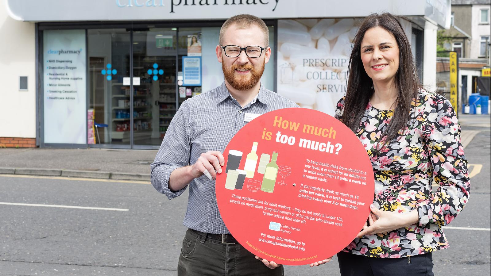 Photograph of Stephanie Hanlon Joint Regional Lead for Drugs and Alcohol, PHA and Pharmacist George Wright, holding the Focus on Alcohol photo prop, outside Clear Pharmacy. 