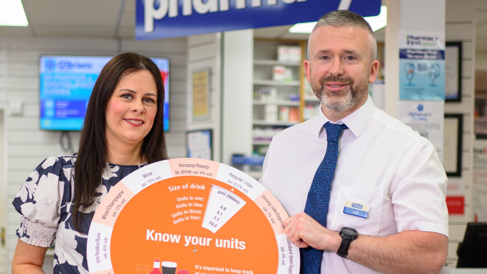 Photograph of PHA rep and pharmacist holding the 'know your units' alcohol wheel in pharmacy. 