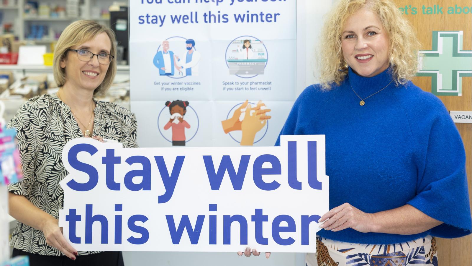 Pharmacist Joyce and Wedny from the PHA hold up a sign saying "Stay Well this Winter"
