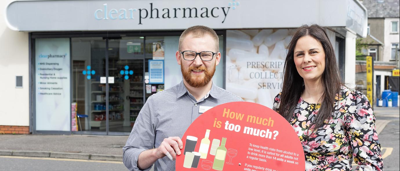 woman and man standing in front of the pharmacy holding information banner about alcohol consumption